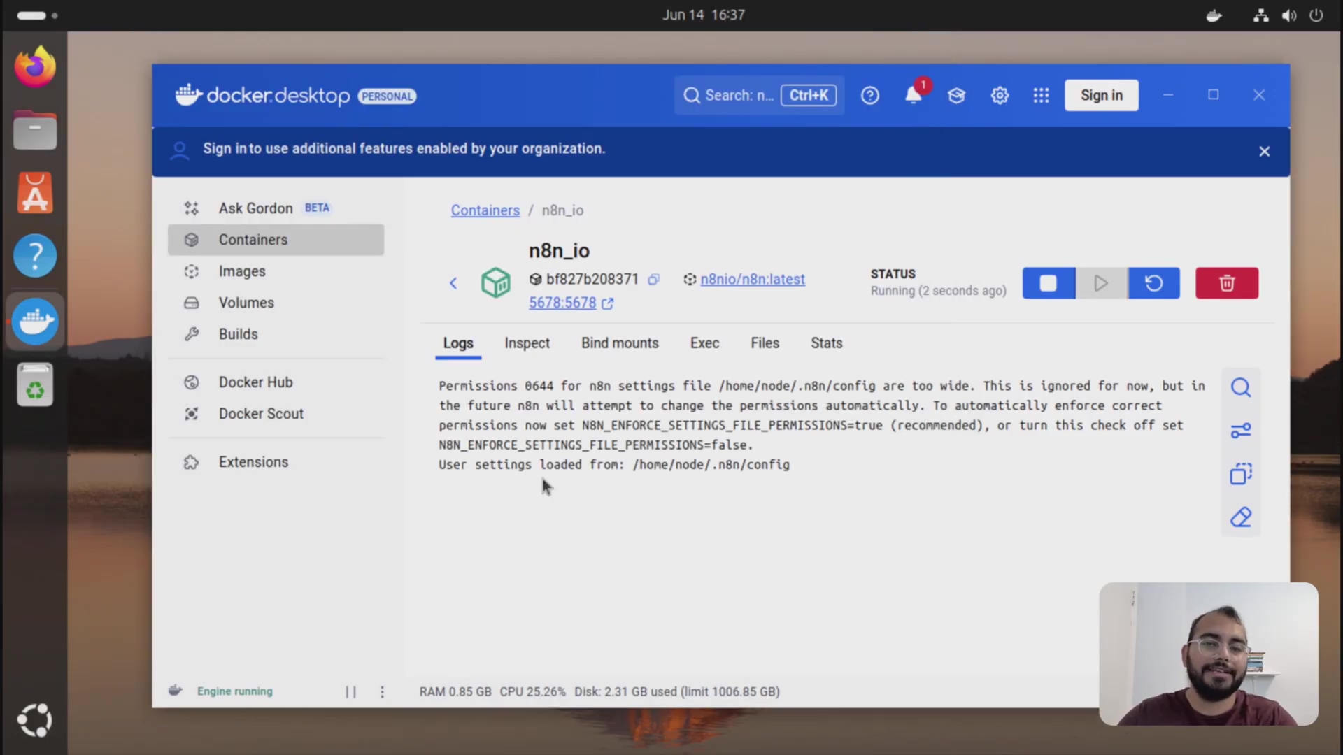 The image displays the Docker Desktop application interface, specifically showing the logs for an 'n8n_io' container. The main panel is divided into tabs: Logs, Inspect, Bind mounts, Exec, Files, and Stats, with 'Logs' currently selected. The log output shows messages related to file permissions and user settings for n8n. A sidebar on the left lists navigation options like 'Containers', 'Images', 'Volumes', 'Builds', 'Docker Hub', 'Docker Scout', and 'Extensions'. At the bottom, a status bar indicates 'Engine running' and displays resource usage: 'RAM 0.85 GB', 'CPU 25.26%', 'Disk: 2.31 GB used (limit 1006.85 GB)'. A person is visible in the bottom right corner, partially obscured by the interface.