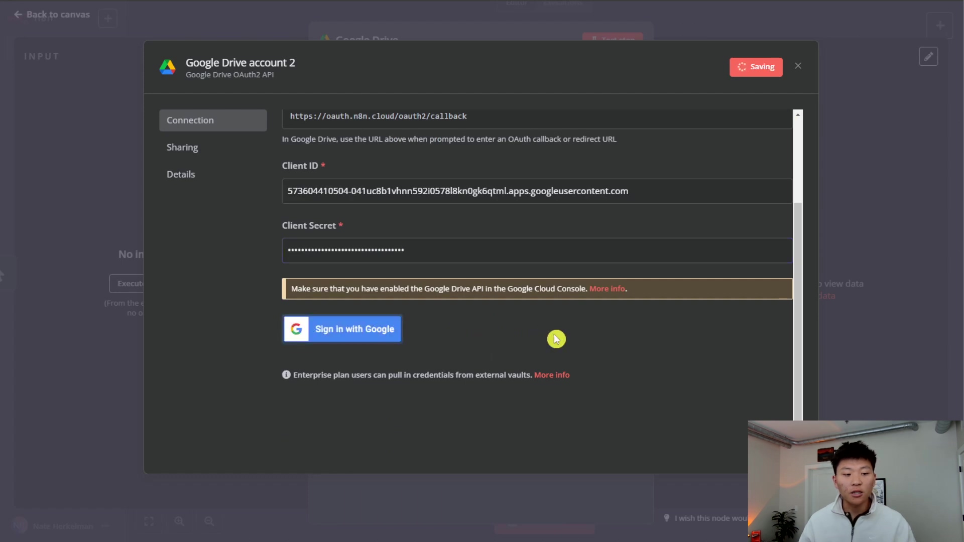 The image shows a pop-up window titled 'Google Drive account 2' within the n8n interface, related to Google Drive OAuth2 API. The pop-up has tabs for 'Connection', 'Sharing', and 'Details'. The 'Connection' tab is active and displays a URL field, a 'Client ID' field with a long alphanumeric value, and a 'Client Secret' field with masked characters. A warning message states, 'Make sure that you have enabled the Google Drive API in the Google Cloud Console. More info.' Below this, there's a 'Sign in with Google' button. A person is visible in the bottom right corner, looking at the screen.
