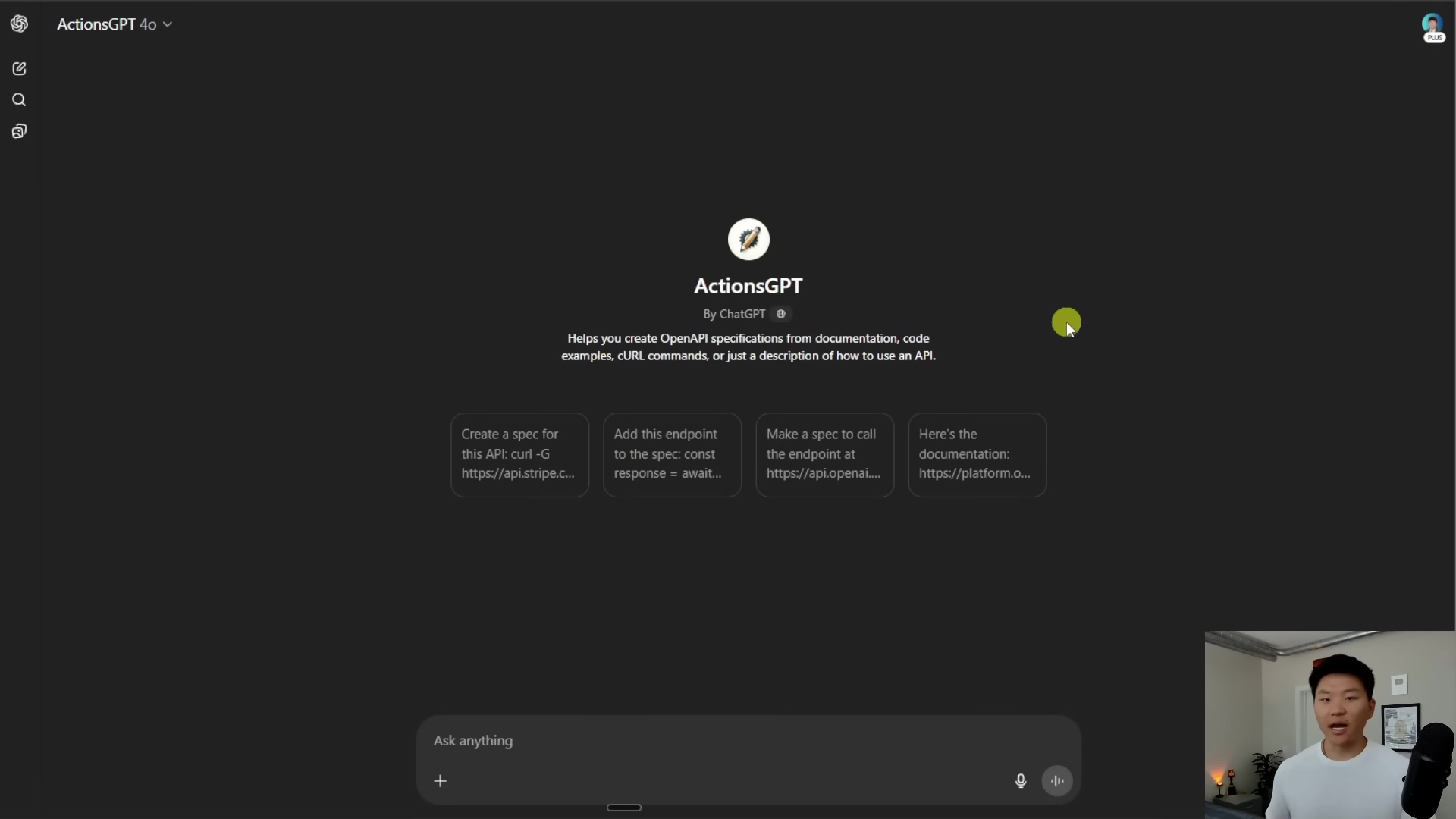 The image displays the 'ActionsGPT' interface within ChatGPT. The main screen is dark gray with a central white box containing the 'ActionsGPT' logo and text. The text reads 'ActionsGPT By ChatGPT' followed by 'Helps you create OpenAPI specifications from documentation, code examples, cURL commands, or just a description of how to use an API.'. Below this, there are three white rectangular buttons with text: 'Create a spec for this API: curl -G https://api.stripe.c...', 'Add this endpoint to the spec: const response = await...', and 'Make a spec to call the endpoint at https://api.openai...'. A fourth button, 'Here's the documentation: https://platform.o...', is partially visible on the right. At the bottom of the screen, there is an 'Ask anything' input field with a microphone icon and a keyboard icon. A person is visible in the bottom right corner of the screen, looking at the camera.