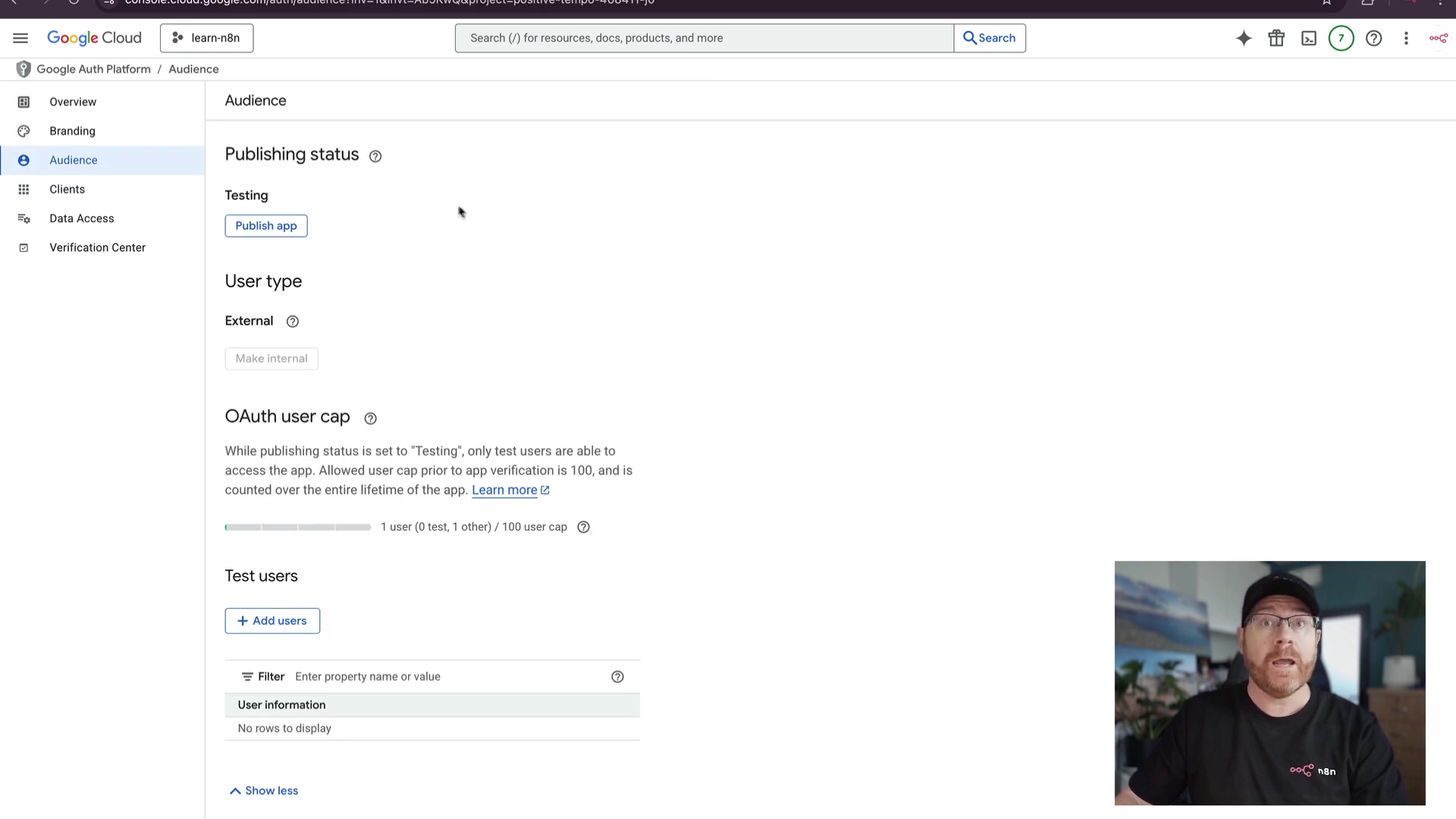 The image displays a Google Cloud Platform interface focused on the OAuth consent screen's 'Audience' section. On the left, a navigation panel shows options like 'Overview', 'Branding', 'Audience', 'Clients', 'Data Access', and 'Verification Center', with 'Audience' highlighted. The main content area shows 'Publishing status' as 'Testing' with a 'Publish app' button. Below that, 'User type' is set to 'External' with a 'Make internal' button. Further down, 'OAuth user cap' indicates '1 user (0 test, 1 other) / 100 user cap' with a 'Learn more' link. A 'Test users' section has a '+ Add users' button and a filter input field. The bottom right corner of the screen shows a man with glasses and a beard, wearing a black t-shirt with a white logo, looking towards the screen. His presence indicates a demonstration or tutorial context.