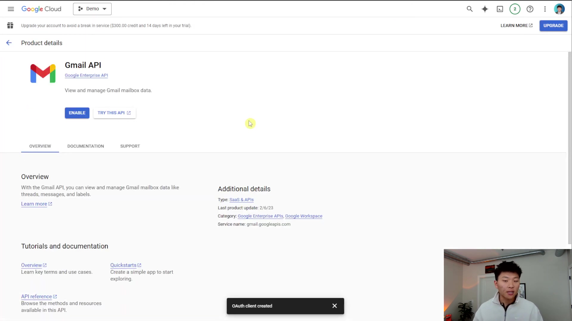 The image displays the Google Cloud console, specifically the 'Product details' page for the 'Gmail API'. The page shows an overview of the API, stating 'View and manage Gmail mailbox data'. There are 'ENABLE' and 'TRY THIS API' buttons. The right side shows 'Additional details' including 'Type: SaaS & APIs', 'Last product update: 2/6/23', 'Category: Google Enterprise APIs, Google Workspace', and 'Service name: gmail.googleapis.com'. Below the main content, a black pop-up notification reads 'OAuth client created'. A person is visible in the bottom right corner, looking at the screen.