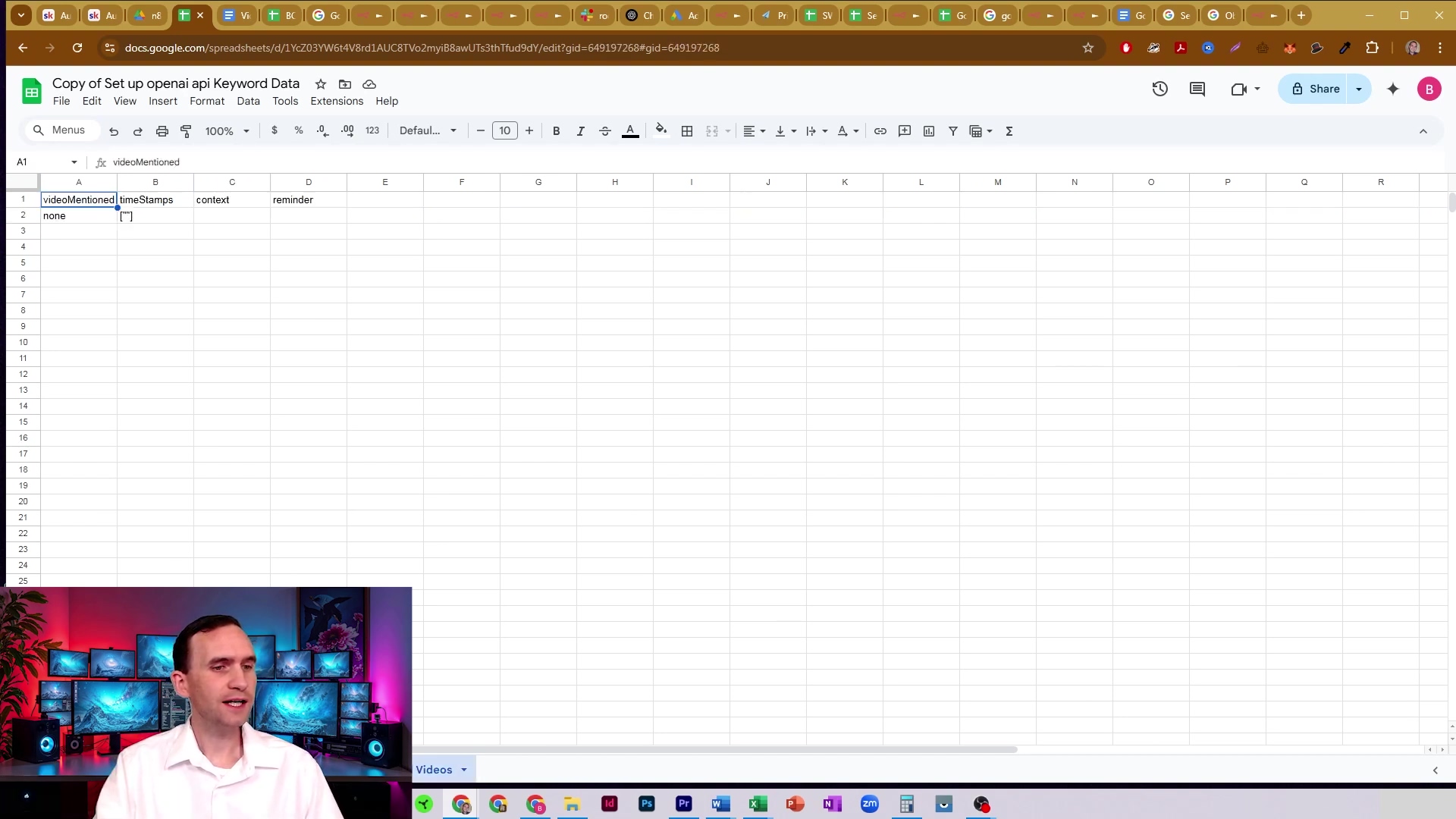 The image shows a Google Sheets document titled "Copy of Set up openai api Keyword Data." The spreadsheet contains columns labeled "videoMentioned," "timeStamps," "context," and "reminder." The first row under "videoMentioned" has "none" entered. The sheet is largely empty, indicating a placeholder or a sheet with no data. The standard Google Sheets interface elements are visible at the top, including menu options like "File," "Edit," "View," "Insert," "Format," "Data," "Tools," "Extensions," and "Help." A man is visible in the bottom left corner, speaking, with multiple computer monitors behind him.