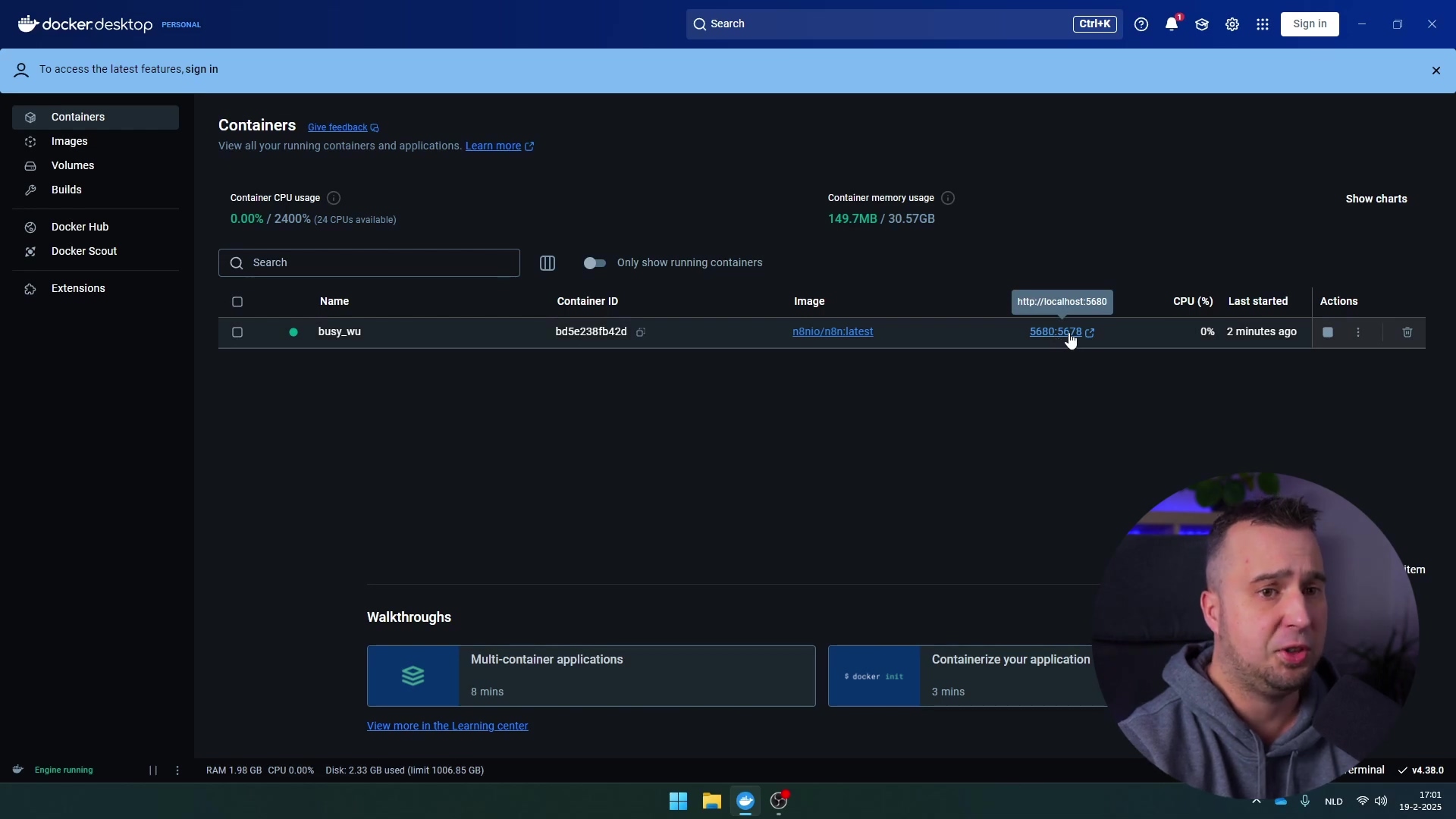 The image displays the Docker Desktop interface, specifically the 'Containers' section, showing a running container named 'busy_wu'. The container details include 'Container ID' (bx5c238f42d), 'Image' (n8nio/n8n:latest), and a 'Ports' column with a clickable link 'http://localhost:5680'. Other columns show 'CPU (%)', 'Last started', and 'Actions'. The CPU usage is '0.00% / 2400%' and memory usage is '149.7MB / 30.57GB'. A checkbox labeled 'Only show running containers' is visible. The left sidebar shows navigation options like 'Containers', 'Images', 'Volumes', 'Local', 'Hub repositories', 'Builds', 'Docker Hub', and 'Extensions'. A man is visible in the bottom right corner, looking at the screen and pointing towards it. The bottom bar shows 'Engine: running', 'RAM 1.52 GB CPU 0.00%', and 'Disk: 2.20 GB used (limit 1006.85 GB)'.