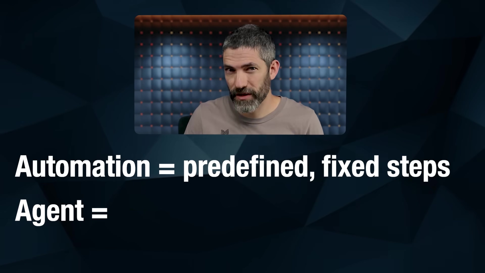 The image presents a comparison between 'Automation' and 'Agent' on a dark blue background with subtle geometric patterns. The text 'Automation = predefined, fixed steps' is displayed in white font. Below it, 'Agent =' is shown, indicating an incomplete definition or a point where the speaker will elaborate. In the upper right corner, a speaker with a beard and short hair is visible, looking directly at the camera. He is wearing a light brown t-shirt and is positioned in front of a dark blue padded wall.