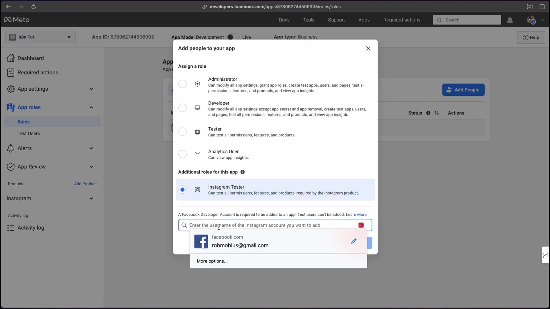 The image shows a pop-up window titled 'Add people to your app' overlaid on the Meta for Developers dashboard. The pop-up presents options to assign a role: 'Administrator', 'Developer', 'Tester', and 'Analytics User', each with a brief description of their permissions. Below these roles, there's a section for 'Additional roles for this app' with 'Instagram Tester' selected. An input field labeled 'Enter the username of the Instagram account you want to add' is visible, with 'robmobius@gmail.com' and 'facebook.com' suggested. The background shows the 'App roles' section of the dashboard with 'Roles' and 'Test Users' sub-options.