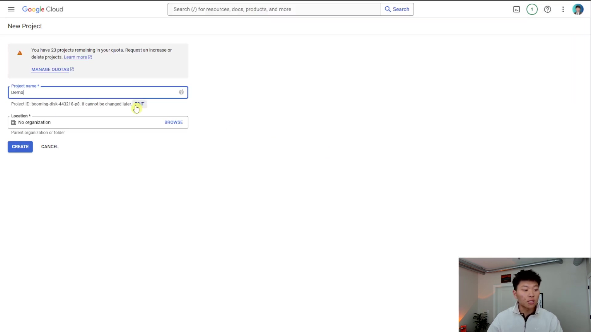 The image shows the Google Cloud 'New Project' creation page. The main section is titled 'New Project' and contains fields for project details. A warning message at the top states: 'You have 23 projects remaining in your quota. Request an increase or delete projects.' with links to 'MANAGE QUOTAS' and 'Learn more'. The 'Project name *' field is filled with 'Demo'. Below it, 'Project ID: booming-disk-442218-p0. It cannot be changed later.' is displayed with a 'COPY' button. The 'Location *' field is set to 'No organization', with a 'BROWSE' button next to it. At the bottom, there are 'CREATE' and 'CANCEL' buttons. A person is visible in the bottom right corner, looking at the screen and gesturing with their hand.