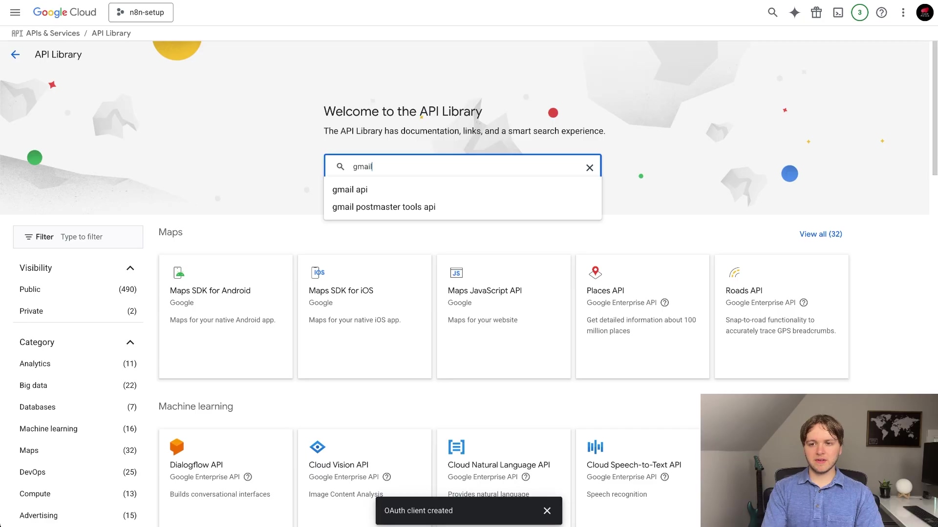 The image displays the Google Cloud API Library interface, specifically showing search results for 'gmail'. The main content area features a 'Welcome to the API Library' message and various API cards, including 'Maps SDK for Android', 'Maps SDK for iOS', 'Maps Javascript API', 'Places API', and 'Roads API'. The search bar at the top right contains 'gmail' with suggestions like 'gmail api' and 'gmail postmaster tools api'. The left sidebar lists categories and their counts, such as 'Visibility' (Public, Private), and 'Category' (Analytics, Big data, Databases, Machine learning, DevOps, Compute, Advertising). A small 'OAuth client created' pop-up is visible at the bottom left. A man is visible in the bottom right corner of the screen, looking at the interface.