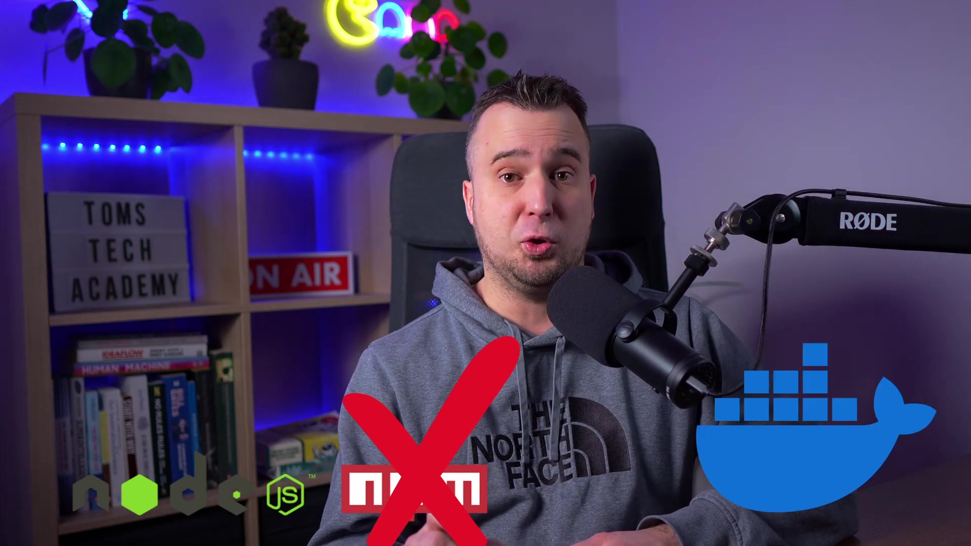 The image shows a man sitting in front of a microphone, looking directly at the camera. He is wearing a grey hoodie with 'THE NORTH FACE' logo. To his left, there is a bookshelf with various books and two signs: 'TOMS TECH ACADEMY' and 'ON AIR'. In the foreground, there are graphic overlays. On the left, there are logos for n8n, node.js, and other tools, with a large red 'X' over them, indicating they are not the preferred method. On the right, there is a large blue Docker whale logo, suggesting it is the recommended method. The background features purple and green neon lights and a plant.
