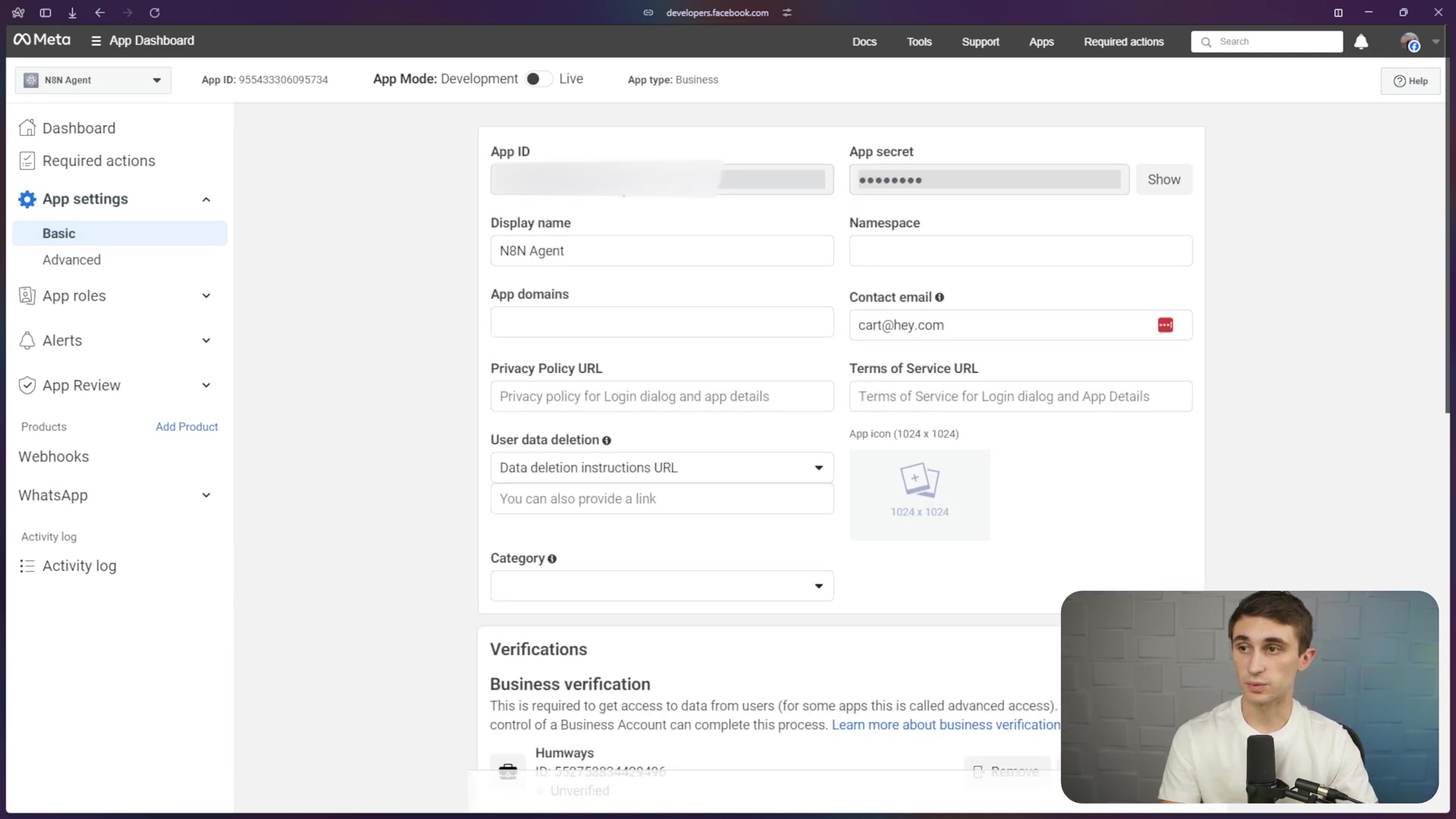 The image displays a Meta App Dashboard interface, specifically the 'App settings' section. On the left sidebar, navigation options like 'Dashboard', 'Required actions', 'App settings' (with 'Basic' and 'Advanced' sub-options highlighted), 'App roles', 'Alerts', 'App Review', 'Products', 'Webhooks', 'Activity log', and 'Activity log' are visible. The main content area shows fields for 'App ID', 'App secret' (partially obscured with 'Show' button), 'Display name' ('N8N Agent'), 'Namespace', 'App domains', 'Contact email' ('cart@hey.com'), 'Privacy Policy URL', 'Terms of Service URL', 'User data deletion URL', and 'Category'. An 'App icon' placeholder is also present. Below these fields, a 'Verifications' section indicates 'Business verification' is required. A man with short dark hair and a light blue shirt is visible in the bottom right corner, looking towards the screen.