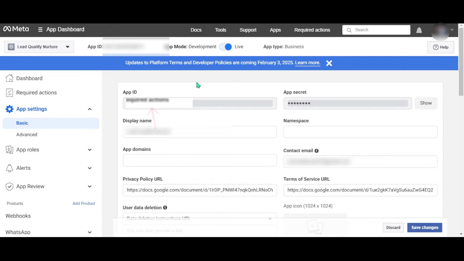 The image displays the 'App settings' section within the Meta App Dashboard, specifically the 'Basic' tab. The main content area shows fields for 'App ID', 'App secret', 'Display name', 'Namespace', 'App domains', and 'Contact email'. The 'App ID' and 'App secret' fields are partially obscured for security, but the 'Show' button for the app secret is visible. Below these, there are fields for 'Privacy Policy URL' and 'Terms of Service URL', both pre-filled with Google Docs URLs. A 'User data deletion instructions URL' field is also present. At the bottom right, 'Discard' and 'Save changes' buttons are visible. A blue banner at the top warns about 'Updates to Platform Terms and Developer Policies' coming February 3, 2025. The left sidebar shows navigation items like 'Dashboard', 'Required actions', 'App settings' (with 'Basic' and 'Advanced' sub-items), 'App roles', 'Alerts', 'App Review', 'Products', 'Webhooks', and 'WhatsApp'. The Meta logo and 'App Dashboard' title are at the top left.