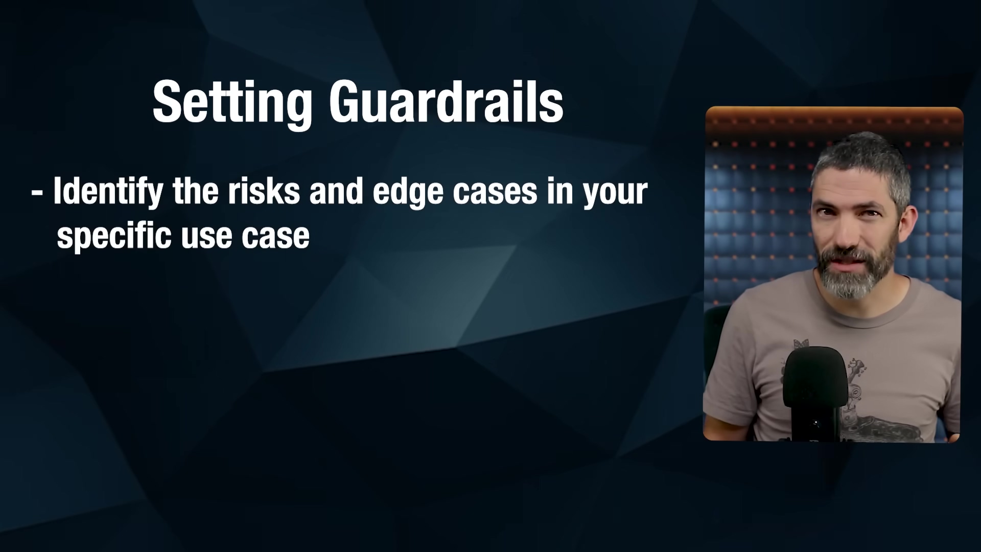 The image shows a man with a beard on the right side of the screen, looking towards the left. He is wearing a grey t-shirt. The left side of the screen features a dark blue background with white text that reads 'Setting Guardrails' as a heading, followed by a bullet point: '- Identify the risks and edge cases in your specific use case'. The background behind the man is dark with blurred lights.