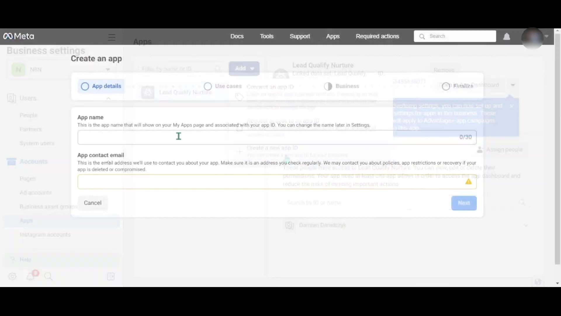 The image displays a Meta Business Suite interface, specifically the 'Create an app' dialog. The dialog is centered on the screen and shows fields for 'App name' and 'App contact email'. The 'App name' field has a placeholder text 'N8 n app' and a character counter '0/30'. Below the 'App contact email' field, there's a warning message about checking the email regularly. On the left sidebar, navigation items like 'Users', 'People', 'Partners', 'System users', 'Accounts', 'Pages', 'Ad accounts', 'Business asset groups', 'Apps', and 'Instagram accounts' are visible. The top navigation bar includes 'Docs', 'Tools', 'Support', 'Apps', 'Required actions', and a search bar. The overall interface is light gray with blue accents for selected elements and buttons. The background shows a blurred view of the business settings.