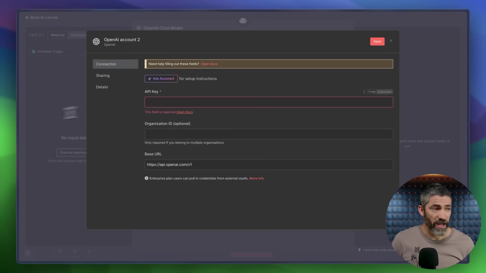 The image displays a configuration panel within a software interface, likely for setting up an OpenAI Chat Model. The panel is titled 'OpenAI Chat Model' and has 'INPUT', 'Mapping', and 'Design' tabs at the top. Below the title, it shows 'OpenAI Account 2' and a 'Save' button. There's a yellow banner with the text 'Need help filling out these fields? Open docs'. The main section contains input fields for 'Connection', 'Sharing', 'Details', 'API Key *', 'Organization ID (optional)', and 'Base URL'. The 'API Key *' field is highlighted in red with the text 'This field is required Open docs'. The 'Base URL' field contains 'https://api.openai.com/v1'. Below this, there's a note: 'Enterprise plan users can pull in credentials from external vaults. More info'. A man is visible in the bottom right corner, looking at the screen.