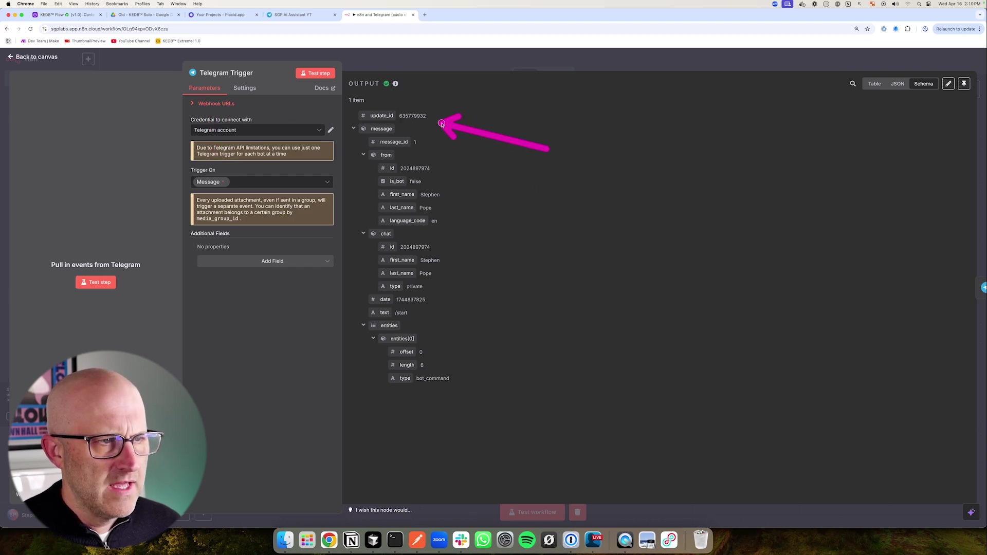 The image shows a screenshot of the n8n workflow interface with a Telegram Trigger node selected. On the left, a man with glasses is partially visible, looking intently at the screen. The Telegram Trigger node's configuration panel is open, displaying fields for 'Credential to connect with Telegram account', 'Trigger On', and 'Additional Fields'. The 'Trigger On' field is set to 'Message'. To the right, an 'OUTPUT' panel shows a JSON structure with details like 'update_id', 'message', 'message_id', 'from' (including 'id', 'is_bot', 'first_name', 'last_name'), 'chat', 'date', 'text', and 'entities'. A large pink arrow points to the 'update_id' field in the OUTPUT panel. The top of the screen shows browser tabs and the n8n application title.