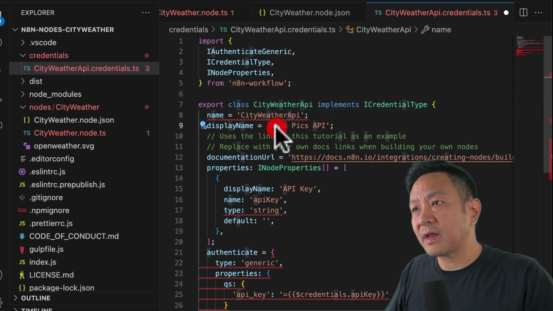The image shows a screen capture of code in an IDE, likely VS Code, with a man's face visible in the lower right corner. The code appears to be related to creating a custom node for n8n, with file names like 'CityWeatherApi.credentials.ts' visible in the file explorer on the left. The code itself includes TypeScript syntax with properties like 'displayName' and 'name'. The man is looking towards the code and appears to be explaining it.
